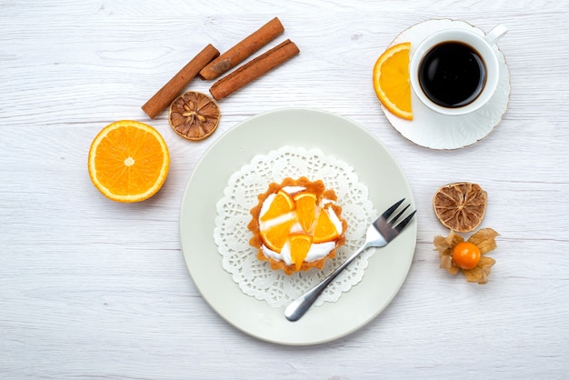 Вид сверху маленького торта со сливками и нарезанными апельсинами вместе с кофе и корицей на светлом столе, фруктовый торт, печенье, сладкий сахар