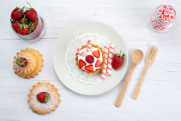 Вид сверху маленького торта со сливками и нарезанной клубникой, торты, конфеты на белом, фруктовый торт, ягодно-сладкий