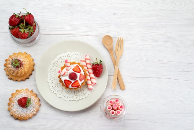 Top view of little cake with cream and sliced strawberries cakes candies on white, fruit cake sweet sugar