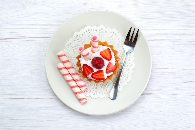 Top view of little cake with cream and sliced strawberries inside plate on white, fruit cake berry sweet sugar