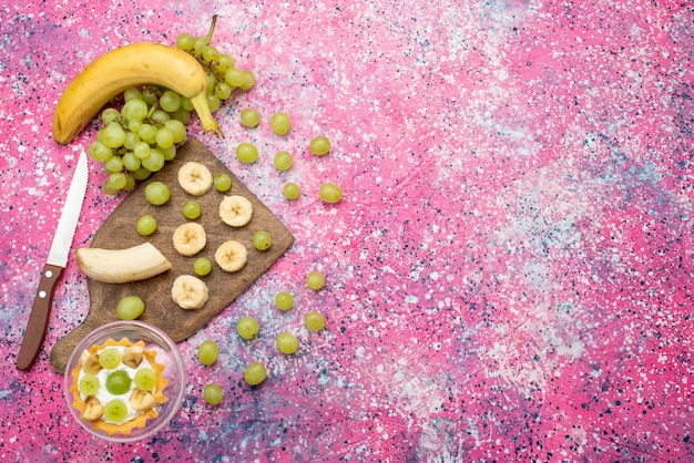 Top view little cake with fresh grapes and bananas on the bright-purple surface fruit cake fresh mellow color