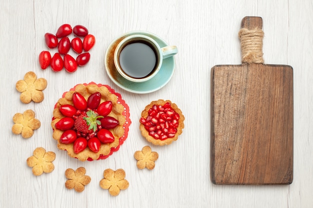 白い机の上にフルーツクッキーとお茶のトップビューの小さなケーキ