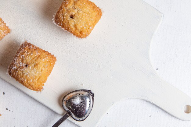 흰색 책상에 설탕 가루와 종이 형태로 구운 작은 케이크의 상위 뷰