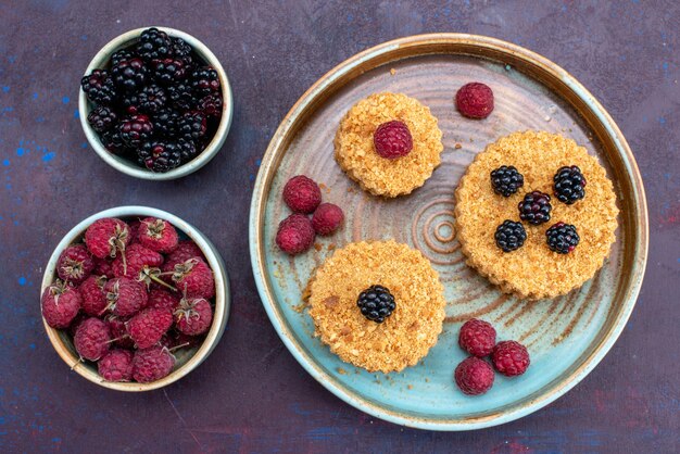 Top view of little cakes sweet and delicious with fresh berries on dark surface