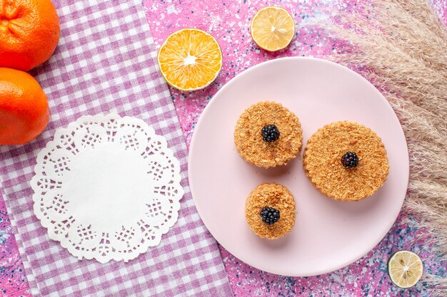 Top view of little cakes with berries inside plate on pink surface