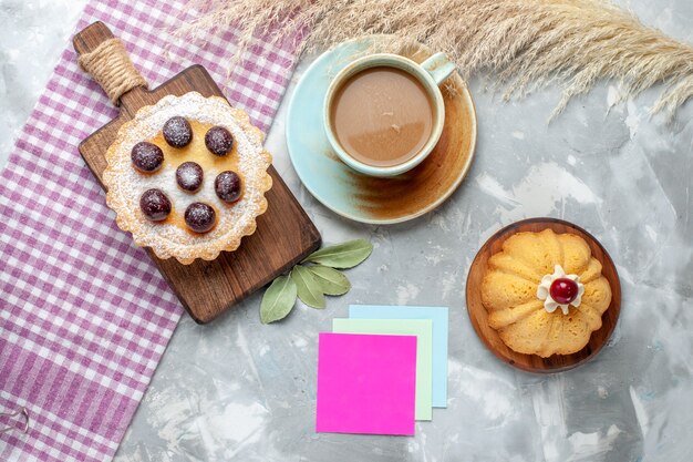 Top view little cakes with fruits along with coffee on the light desk cake biscuit sweet bake