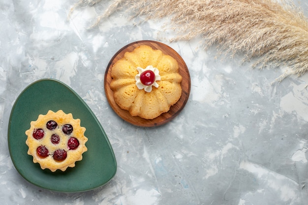 Вид сверху маленькие пирожные с фруктами на светлом столе, бисквитный торт сладкого цвета сахара Бесплатные Фотографии