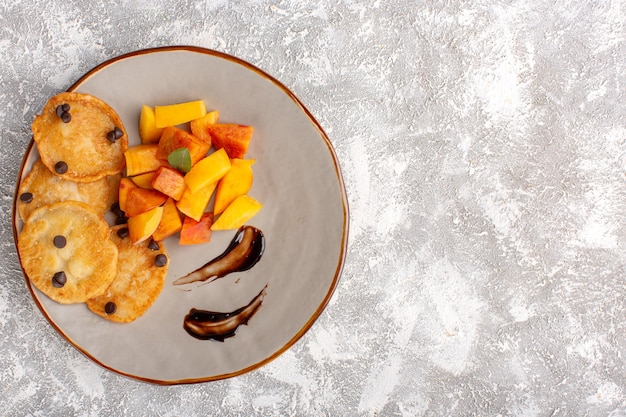 Top view little cookie pastries inside plate with fresh sliced peaches on light table, cake biscuit sweet pastry bake