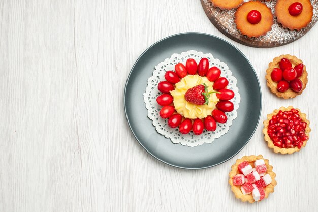 Top view little creamy cake with cakes and fruits on white desk