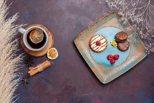 Top view little creamy cake with chocolate cookies and cup of tea on the dark surface biscuit cake sweet pie sugar cookie