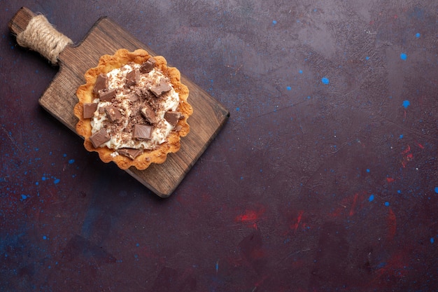 Top view of little creamy cake with chocolate pieces on the dark surface