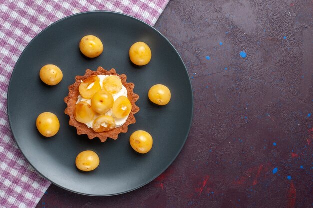 Top view of little creamy cake with fresh sweet cherries inside plate on dark-purple surface