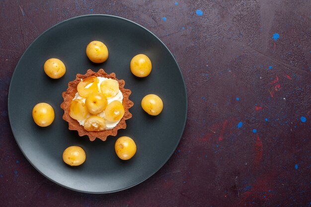 Top view of little creamy cake with fresh sweet cherries inside plate on dark surface