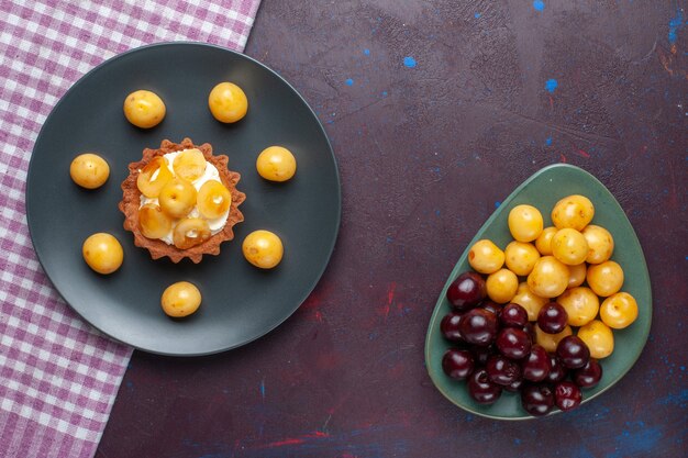 Top view of little creamy cake with fresh sweet cherries inside plate on the dark surface