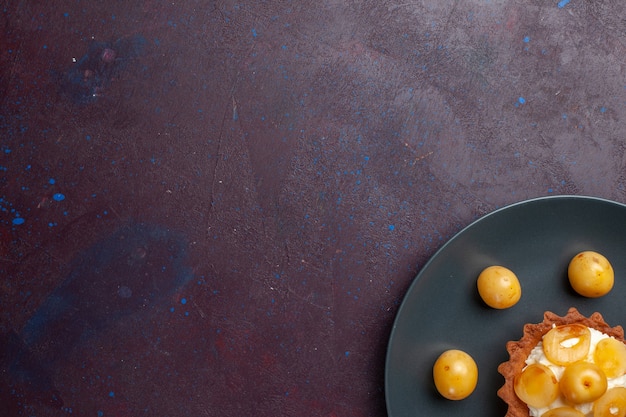 Top view of little creamy cake with fresh sweet cherries inside plate on the dark surface