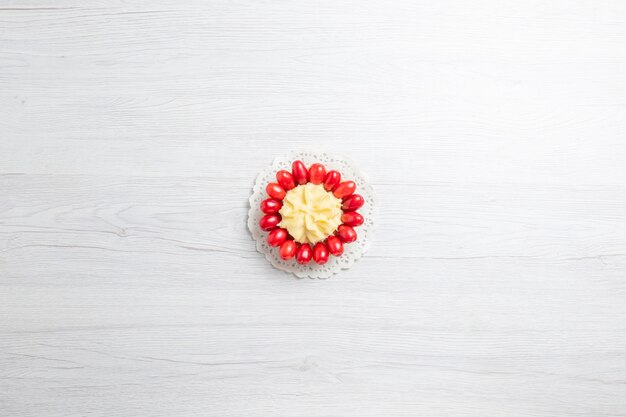 Top view little creamy cake with red dogwoods on a white desk