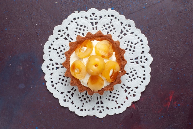 Top view of little creamy cake with sliced fruits on dark surface