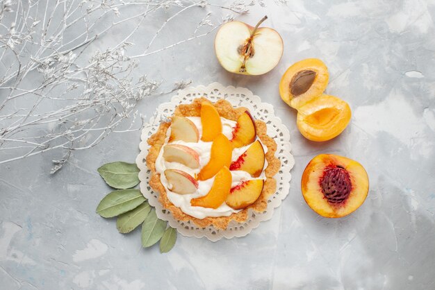 Top view little creamy cake with sliced fruits and white cream along with fresh apricots peaches on the white light desk fruits cake biscuit cookie