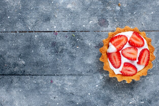 Top view little creamy cake with sliced strawberries on the grey background desk fruit berry cake sweet color