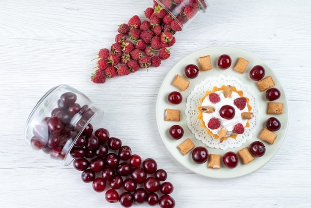 Top view little creamy cake with sour cherries and raspberries on the light-white table fresh fruit berry cake sweet