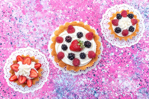 Top view little creamy cakes with different berries on the light white desk cake biscuit berry sweet bake