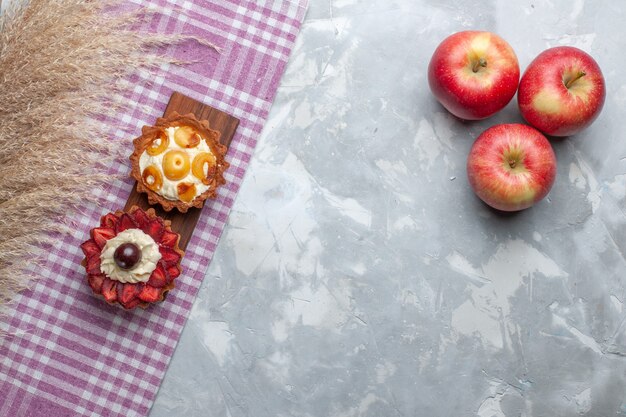 Top view little creamy cakes with fresh red apples on the white desk fruit cake biscuit cream sweet