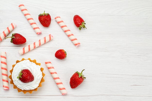 Top view little creamy cakes with fresh strawberries and candies on the light desk cake sweet photo fruit berry bake