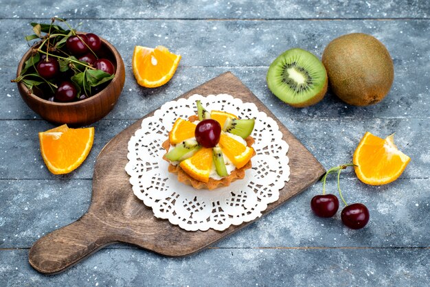 A top view little delicious cake with cream and fresh sliced fruits on the grey desk fruit cake biscuit