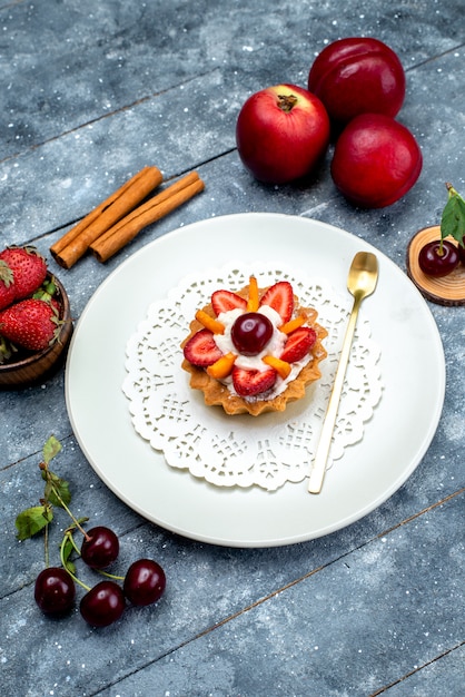 A top view little delicious cake with cream and fruits inside white plate along with fresh fruits on the grey-blue desk fruit cake biscuit 