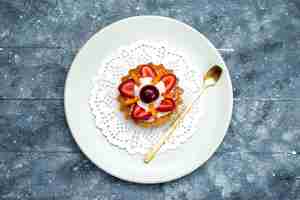 Free photo a top view little delicious cake with cream and fruits inside white plate on the grey-blue desk fruit cake biscuit