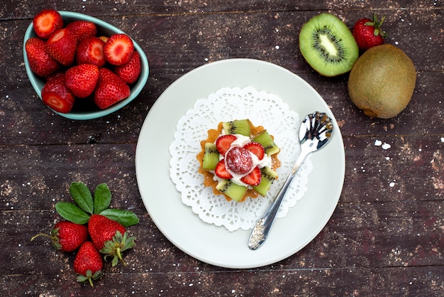 A top view little delicious cake with cream inside plate with fresh strawberries and kiwis on the dark background cookie biscuit cake fruit 