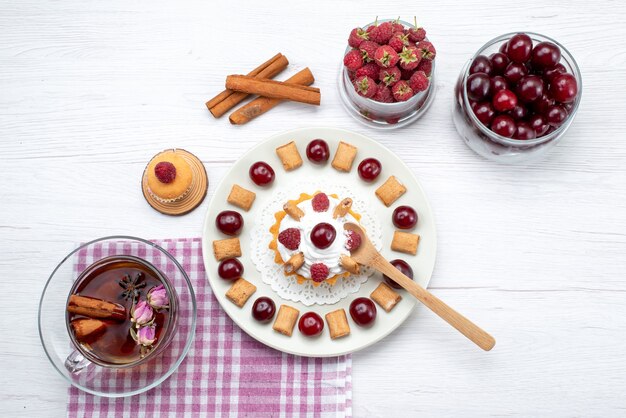 Top view little delicious cake with raspberries cherries and little biscuits tea cinnamon on the white table fruit berry cream tea