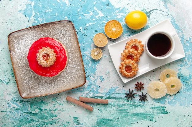 Foto gratuita vista dall'alto piccola deliziosa torta con crema rossa tazza di tè e biscotti su sfondo azzurro torta biscotto dolce torta di zucchero tè