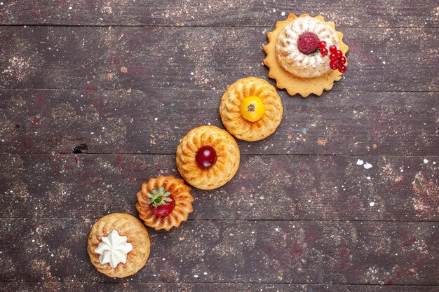 Top view little delicious cakes and cookies with berries on the brown background cake biscuit berry photo cookie