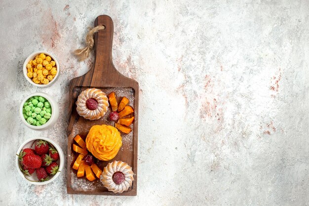 Top view little delicious cakes perfect dessert for tea with candies on light white surface tea pie cake dessert sweet cookies