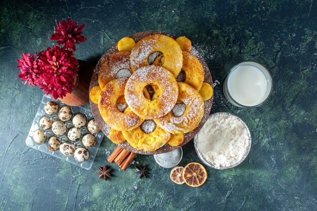Вид сверху маленькие вкусные пирожные в форме кольца ананаса с молоком на темном фоне, горячее пирожное, выпечка, пирог, печенье, торт, фруктовая выпечка