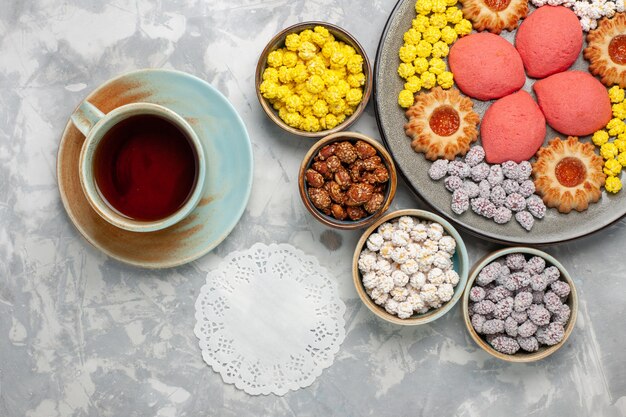 Foto gratuita vista dall'alto piccole deliziose torte con biscotti, tè e caramelle sulla scrivania bianca caramelle dolci biscotti torta torta di zucchero