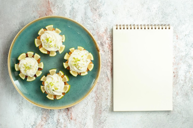 Free photo top view little delicious cakes with cream and lemon slices on light white surface cake biscuit cookie sweet tea sugar