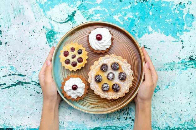 Top view little delicious cakes with cream on the light-blue table cake biscuit sweet tea cream