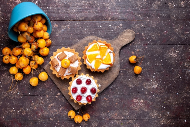 Foto gratuita vista dall'alto piccole deliziose torte con crema di frutta a fette e ciliegie fresche gialle sullo sfondo di legno marrone torta di frutta fresca biscotto dolce