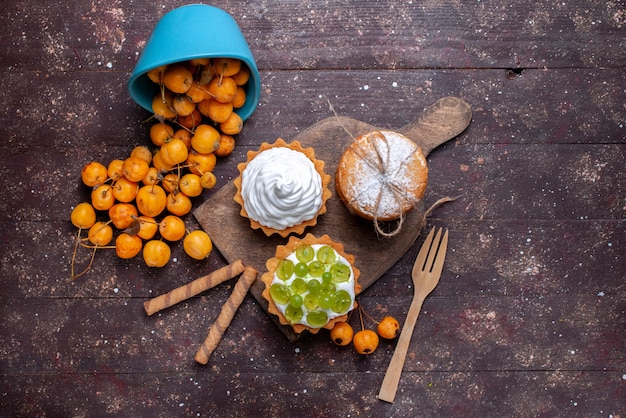 Free photo top view little delicious cakes with cream sliced grapes cookie and fresh yellow cherries on the brown desk fresh fruit cake biscuit sweet cherry