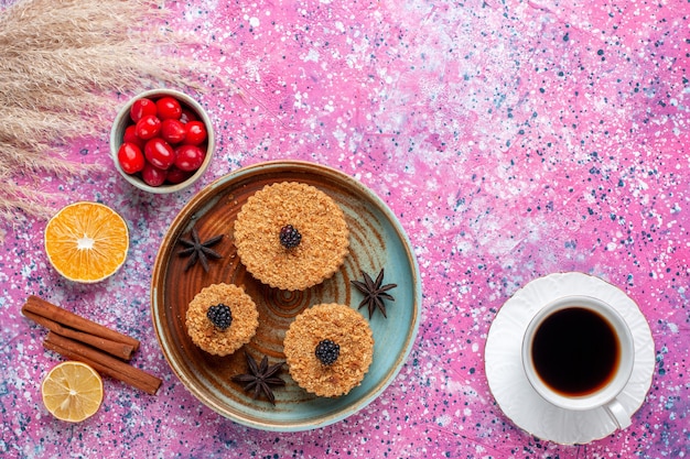 Vista dall'alto di piccole deliziose torte con cornioli e tè sulla superficie rosa chiaro