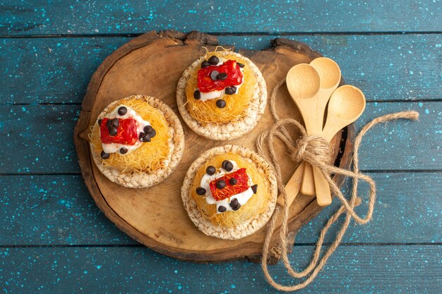 Top view of little delicious cakes with fruits on the brown wooden board and blue surface