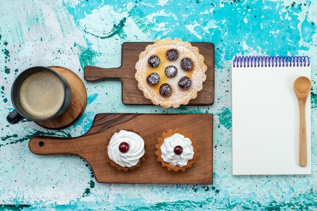 Top view little delicious cakes with fruits milk and notepad on the light-blue background cake sweet sugar cream color photo