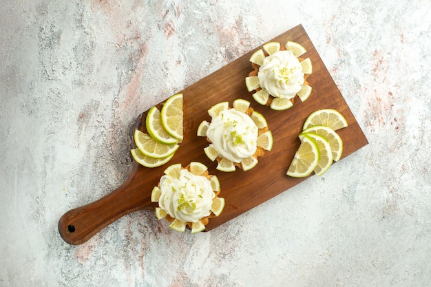 Foto gratuita vista dall'alto piccole deliziose torte con fette di limone su superficie bianca torta biscotto biscotto dolce crema di tè zucchero cream