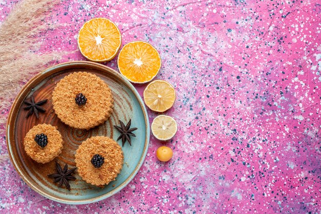 분홍색 표면에 오렌지 조각과 작은 맛있는 케이크의 상위 뷰