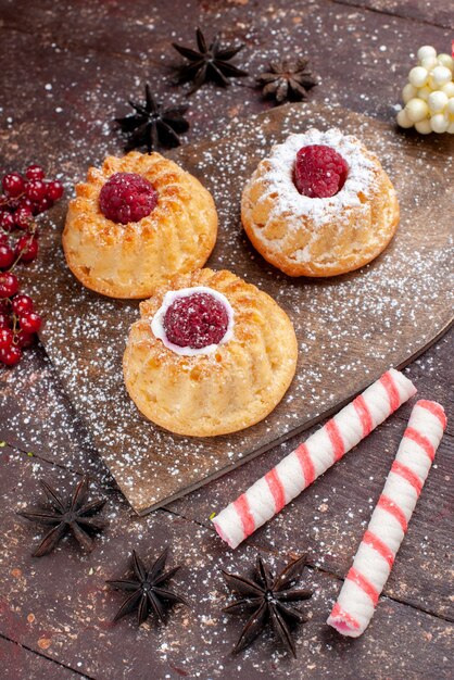 Top view little delicious cakes with raspberries along with stick candies on the wooden desk cake sweet fruit biscuit berry