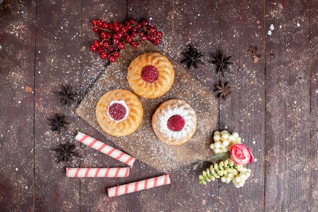 Top view little delicious cakes with raspberries and fresh cranberries along with stick candies on the wooden desk cake sweet sugar fruit