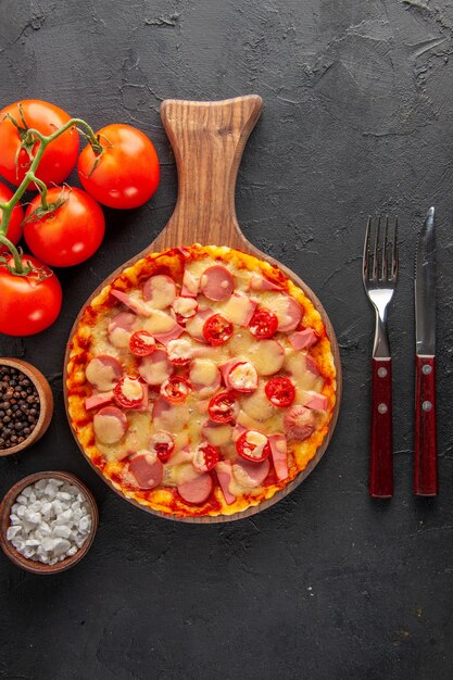 Top view little delicious pizza with tomatoes and cutlery on a dark table