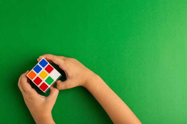 Top view little kid playing with rubics cube on green surface